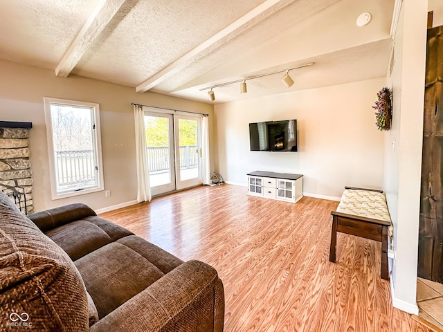 living room with baseboards, light wood finished floors, rail lighting, a textured ceiling, and beamed ceiling