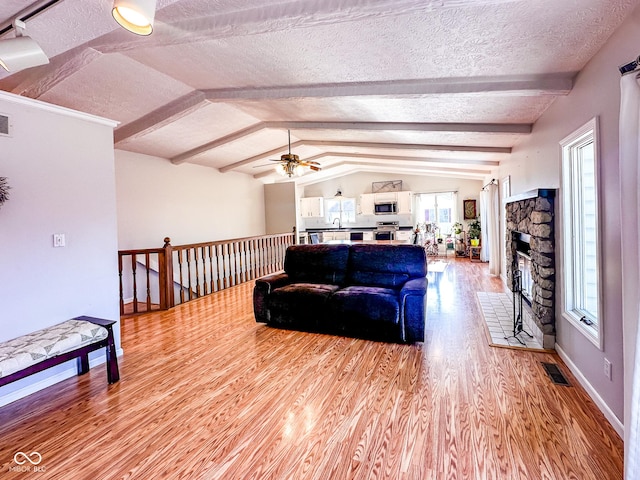 living area featuring visible vents, lofted ceiling with beams, light wood-style flooring, a fireplace, and a textured ceiling