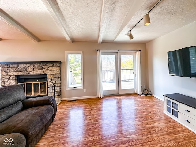 living room featuring baseboards, beam ceiling, a fireplace, wood finished floors, and a textured ceiling