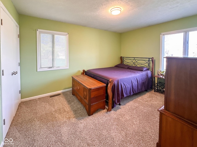 bedroom with visible vents, light carpet, a textured ceiling, and baseboards