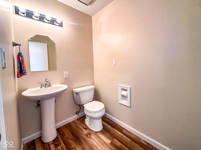 half bathroom with a sink, toilet, baseboards, and wood finished floors