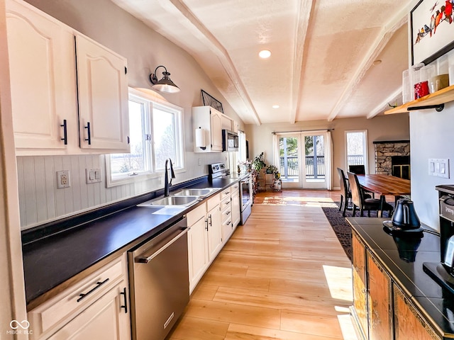 kitchen with beam ceiling, a sink, light wood-style floors, appliances with stainless steel finishes, and dark countertops