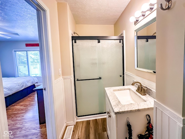 bathroom featuring vanity, wood finished floors, a wainscoted wall, a stall shower, and a textured ceiling