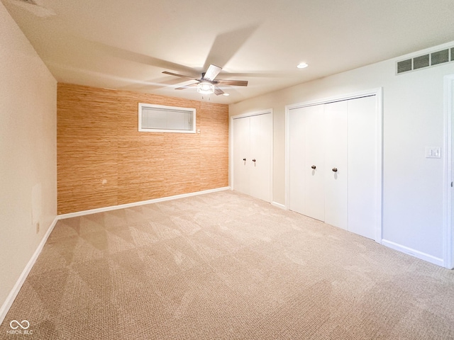 unfurnished bedroom featuring wooden walls, a ceiling fan, visible vents, carpet floors, and two closets