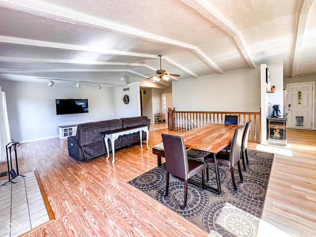 dining room featuring light wood-style flooring, a textured ceiling, vaulted ceiling with beams, and ceiling fan