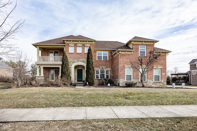 view of front facade with stone siding, a front yard, a balcony, and brick siding