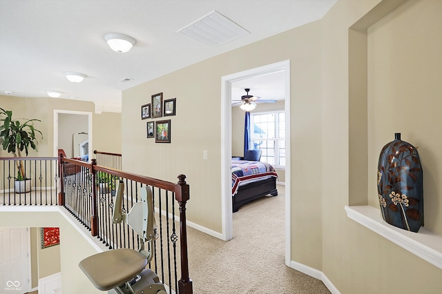 hallway with an upstairs landing, visible vents, carpet flooring, and baseboards