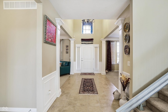 entrance foyer featuring stairway, a wainscoted wall, visible vents, decorative columns, and a notable chandelier