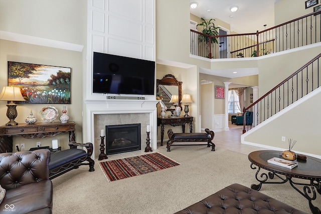 carpeted living area with stairway, a high ceiling, a wainscoted wall, and a fireplace