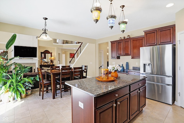 kitchen with a center island, dark stone counters, light tile patterned floors, hanging light fixtures, and stainless steel fridge