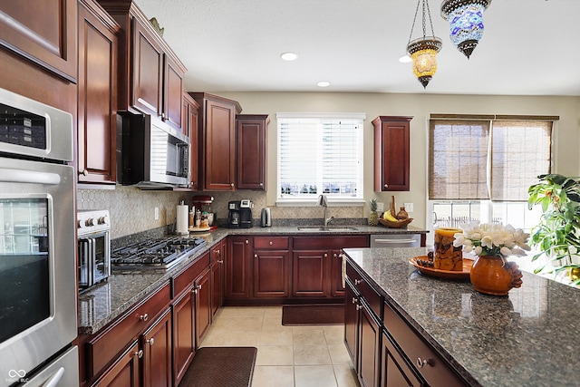 kitchen featuring light tile patterned floors, stainless steel appliances, a sink, reddish brown cabinets, and backsplash