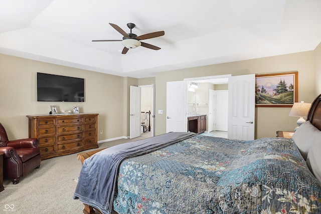 carpeted bedroom with connected bathroom, a tray ceiling, baseboards, and ceiling fan