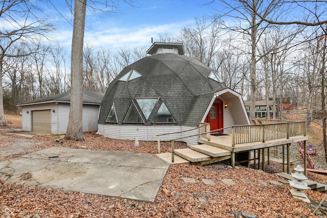 view of front of home featuring a gambrel roof, an outbuilding, a garage, a shingled roof, and a wooden deck