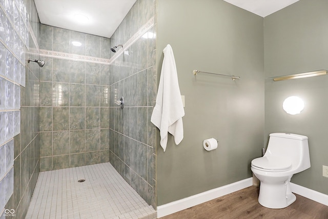 full bath featuring toilet, wood finished floors, baseboards, and tiled shower