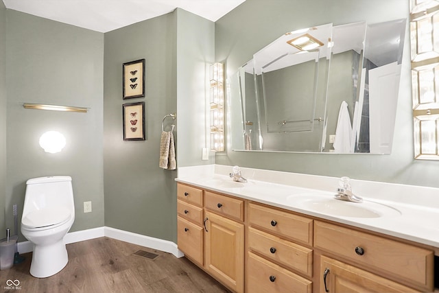 bathroom featuring wood finished floors, baseboards, double vanity, a sink, and toilet