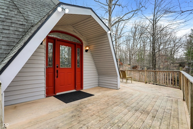 view of exterior entry featuring a wooden deck and roof with shingles