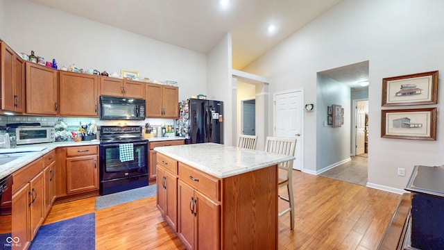 kitchen featuring high vaulted ceiling, a breakfast bar, black appliances, light wood-style floors, and backsplash