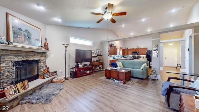 living room featuring light wood-style flooring, a fireplace, a textured ceiling, and lofted ceiling