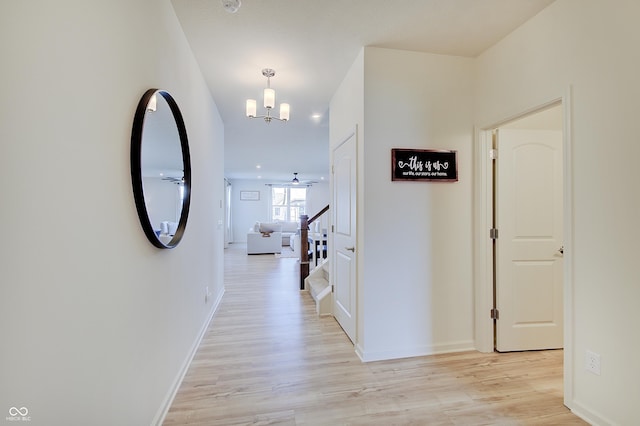 hallway with baseboards, light wood-type flooring, and a chandelier