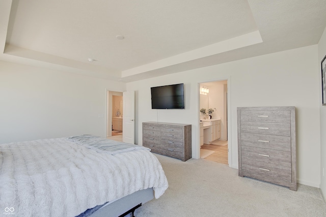 bedroom with a tray ceiling, light carpet, and ensuite bathroom