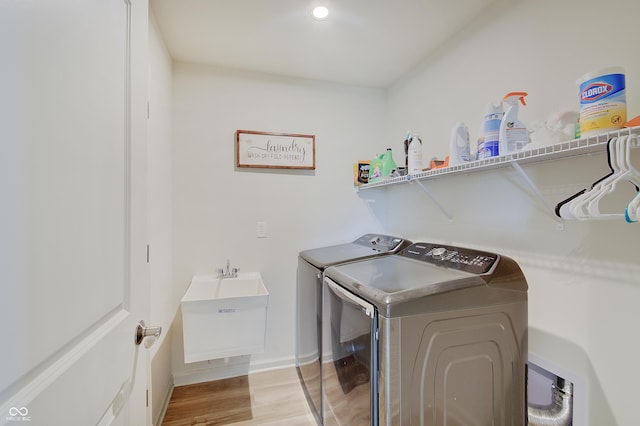 clothes washing area featuring a sink, washing machine and dryer, light wood-style floors, baseboards, and laundry area