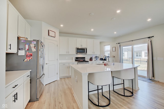 kitchen with a breakfast bar area, light wood-type flooring, an island with sink, appliances with stainless steel finishes, and white cabinetry