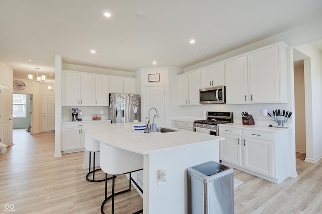 kitchen with a kitchen bar, light wood-type flooring, a center island with sink, a sink, and appliances with stainless steel finishes