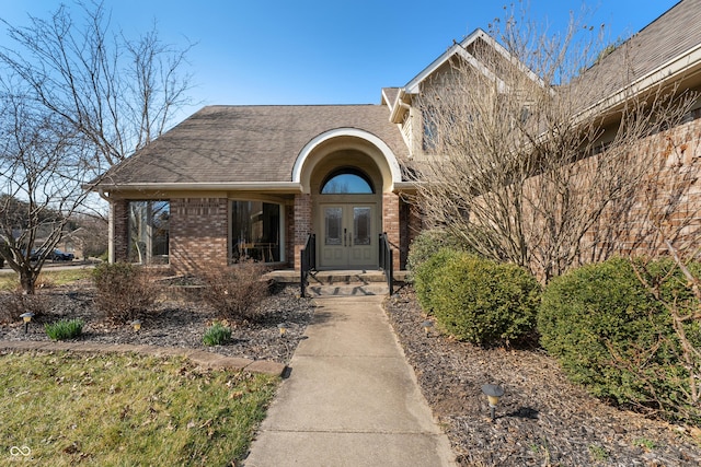 property entrance featuring brick siding, french doors, and a shingled roof