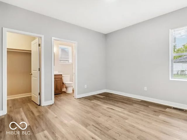 unfurnished bedroom with visible vents, baseboards, light wood finished floors, a closet, and a walk in closet