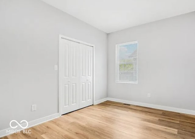 unfurnished bedroom featuring a closet, light wood-type flooring, and baseboards