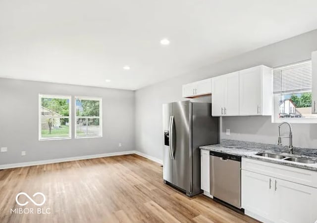 kitchen featuring light stone counters, light wood-style floors, white cabinets, stainless steel appliances, and a sink