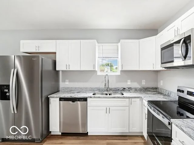 kitchen with light stone countertops, a sink, stainless steel appliances, white cabinets, and light wood-type flooring