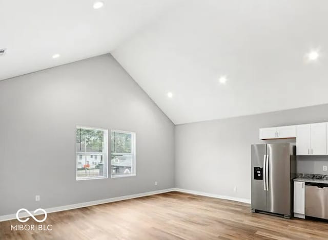 interior space with white cabinetry, baseboards, light wood-style flooring, stainless steel appliances, and high vaulted ceiling