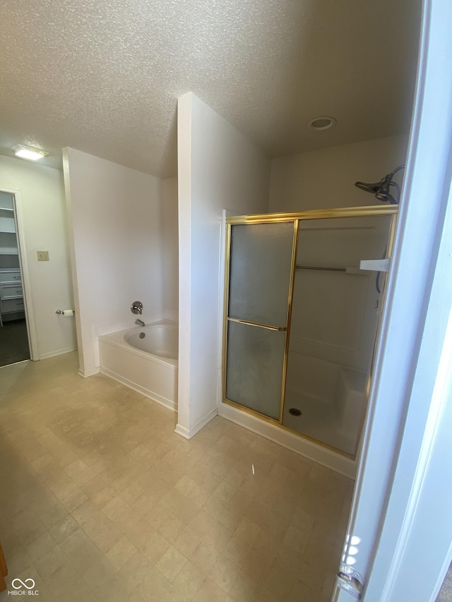 bathroom with baseboards, a stall shower, a textured ceiling, tile patterned floors, and a bath