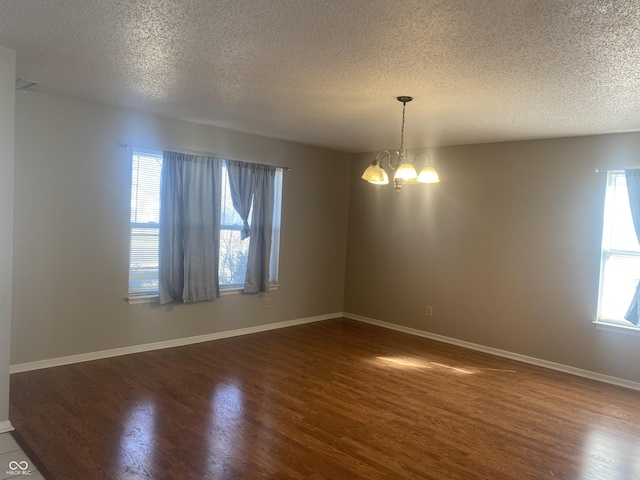 empty room featuring a notable chandelier, a textured ceiling, dark wood-type flooring, and baseboards