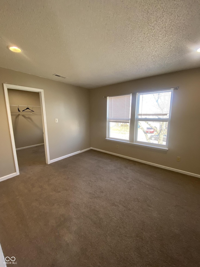 empty room with dark colored carpet, visible vents, baseboards, and a textured ceiling