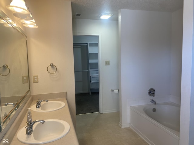 bathroom with a sink, a garden tub, a textured ceiling, and a walk in closet