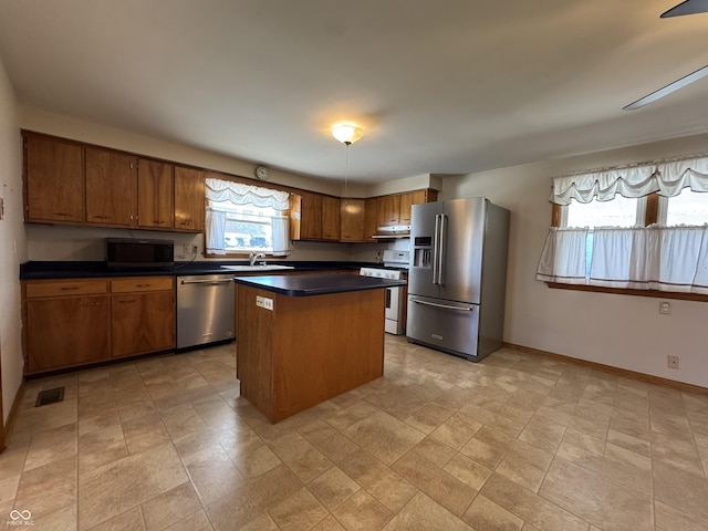 kitchen with dark countertops, visible vents, a kitchen island, appliances with stainless steel finishes, and a sink