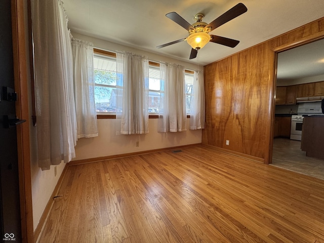 unfurnished room with light wood-style flooring, a ceiling fan, baseboards, and wood walls