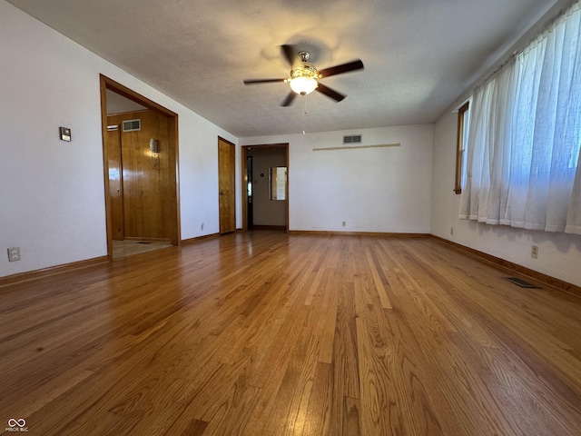 empty room with visible vents, ceiling fan, and wood finished floors