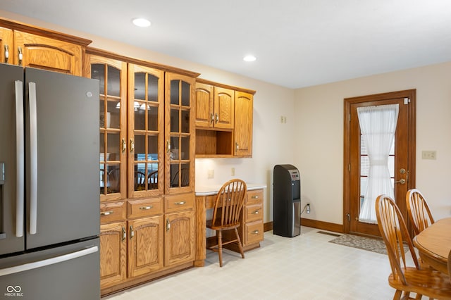 kitchen with brown cabinetry, built in study area, glass insert cabinets, and stainless steel fridge with ice dispenser