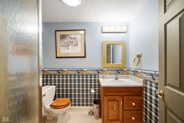 bathroom featuring tile patterned flooring, wallpapered walls, a wainscoted wall, toilet, and a textured ceiling