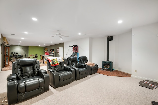 home theater featuring baseboards, light carpet, recessed lighting, a wood stove, and a ceiling fan