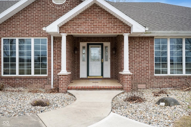 doorway to property with brick siding and a shingled roof