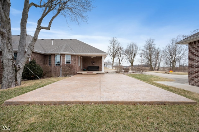 back of house with brick siding, a yard, a shingled roof, and a patio