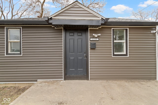 view of exterior entry with roof with shingles