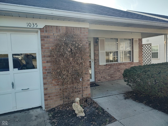 view of exterior entry featuring a porch, brick siding, and roof with shingles