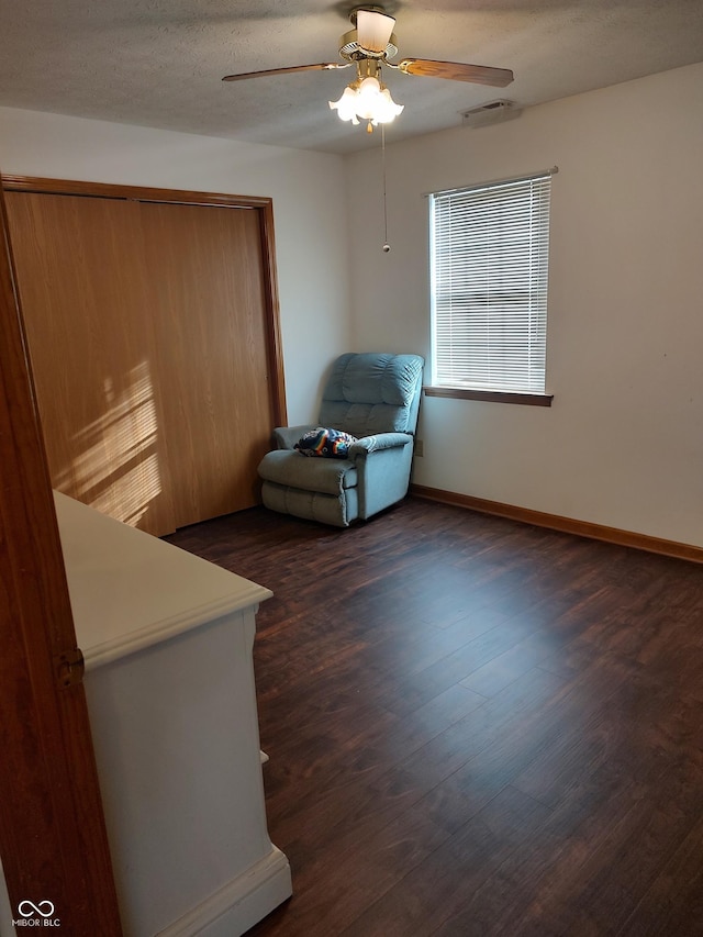 interior space with a ceiling fan, visible vents, baseboards, dark wood finished floors, and a textured ceiling