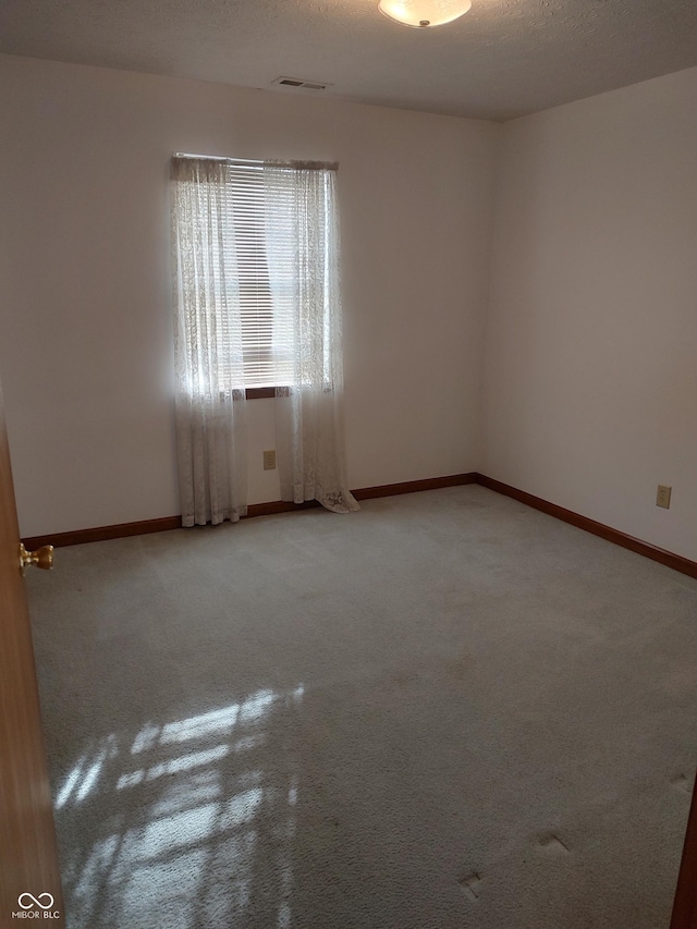 unfurnished room featuring visible vents, baseboards, a textured ceiling, and light carpet