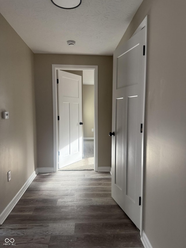 hallway featuring dark wood finished floors, a textured ceiling, and baseboards